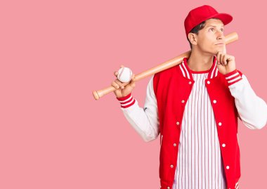 Beyzbol sopasıyla top oynayan yakışıklı genç adam ciddi bir yüz ifadesiyle eli çenesinde soru soran, kafa karıştırıcı bir fikir hakkında düşünceli. 