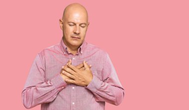 Orta yaşlı kel bir adam, sıradan kıyafetler giyiyor, elleri göğsünde, gözleri kapalı gülümsüyor ve yüzünde minnet ifadesi var. sağlık kavramı. 