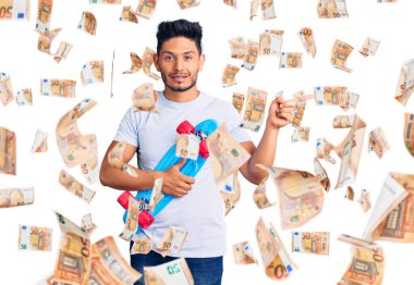 Yakışıklı Latin Amerikalı genç kaykaycı. Gülümsüyor. Elleri ve parmakları yana doğru uzanıyor.