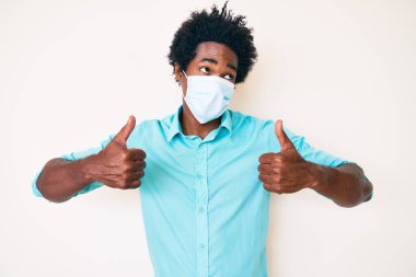 Yakışıklı, Afro saçlı, tıbbi maske takan, gülümseyen ve kafasını çeviren Afro-Amerikan bir adam.. 