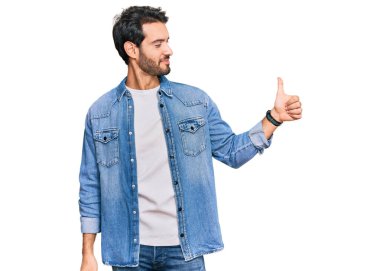 Latin asıllı, sıradan kıyafetler giyen, gururlu, gülümseyen, baş parmak kaldıran genç bir adam. 