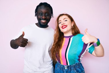 Irklar arası çiftler gündelik giysiler giyip mutlu mesut el hareketi yapıyorlar. Kameraya bakıp başarıyı gösteren ifade. 