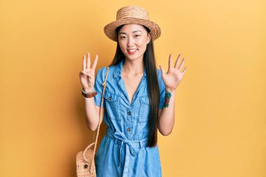 Genç Çinli kadın yaz şapkası takıyor ve 8 numaralı parmaklarıyla işaret ediyor. Bu arada kendinden emin ve mutlu gülümsüyor.. 