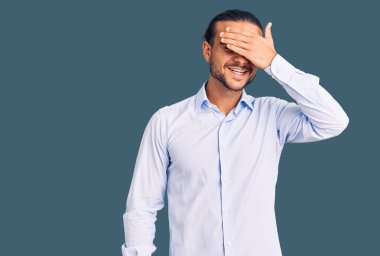 İş kıyafetleri giymiş, gülümseyen ve gülümseyen genç, yakışıklı bir adam şaşırtmak için gözlerini kapatıyor. kör kavram. 