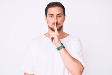 Gündelik beyaz tişört giyen genç yakışıklı dudakları parmaklarıyla sessiz olmak istiyor. sessizlik ve gizli konsept. 
