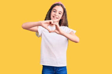 Sevimli İspanyol çocuk günlük beyaz t-shirt 'ler giyiyor. Sevgiyle gülümsüyor. Elleriyle kalp sembolü yapıyor. romantik kavram. 