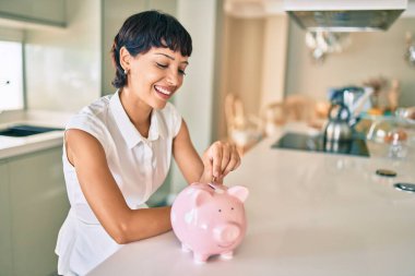 Genç esmer kadın gülümsüyor mutlu bir şekilde kumbaranın içine para koyuyor