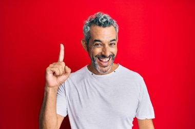 Orta yaşlı, beyaz tişört giyen gri saçlı bir adam başarılı bir fikirle işaret ediyor. Heyecanlı ve mutlu. Bir numara.. 