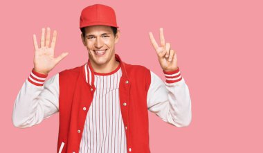 Beyzbol üniforması giyen yakışıklı beyaz adam yedi numarayı gösterip işaret ederken kendinden emin ve mutlu bir şekilde gülümsüyor.. 