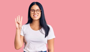 Genç, güzel Asyalı bir kız günlük kıyafetler ve gözlük takıyor. Dört numaralı parmaklarıyla işaret ediyor. Kendinden emin ve mutlu gülümsüyor.. 