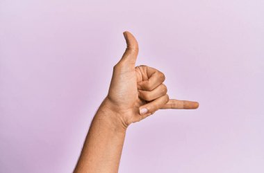 Beyaz bir gencin kolları ve elleri pembe izole edilmiş arka planda. Hawai Shaka selamlama jesti, telefon ve iletişim sembolü. 