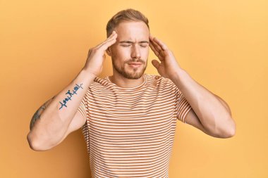 Kafkasyalı genç bir adam, sıradan çizgili tişört giyiyor, eli başının üstünde, stresten baş ağrısı çekiyor. migren ağrısı. 