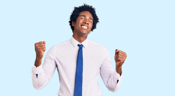 ビジネス服を着てアフロの髪を持つハンサムなアフリカ系アメリカ人男性は非常に満足し 腕を上げて勝者のジェスチャーを行う興奮し 笑顔と成功のために叫んでいます お祝いのコンセプト — ストック写真