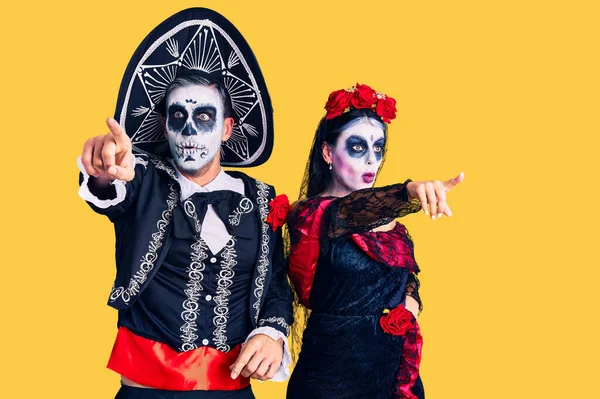 若いカップル身に着けているメキシコの日の死者の衣装を背景に指を前に驚いて 口を開けて驚くような表情 何かを前に — ストック写真