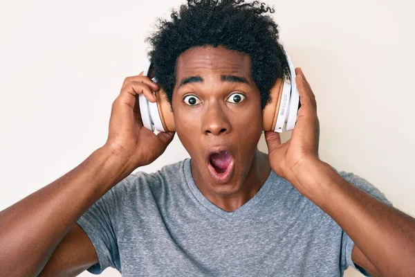 一个英俊的非洲裔美国男人 头发是非洲裔 用耳机听音乐 他害怕 惊讶的表情 兴奋的脸使他震惊 — 图库照片