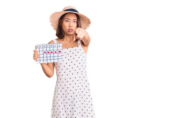 若い美しい中国の女の子を身に着けている夏の帽子心のカレンダーを保持すると指差す指でカメラとあなたに 自信を持ってジェスチャーを真剣に見て — ストック写真