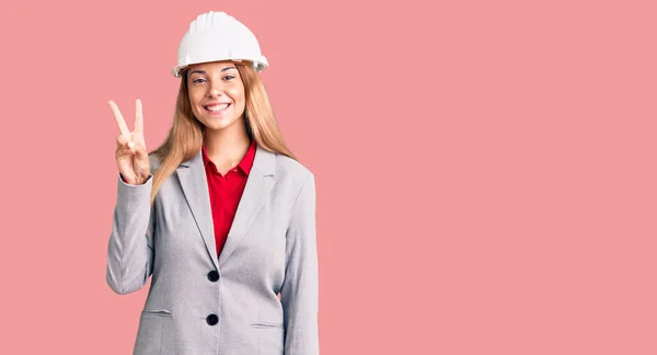 漂亮的年轻女子戴着建筑师的硬礼帽 带着自信和快乐地微笑着 用手指着二号 — 图库照片