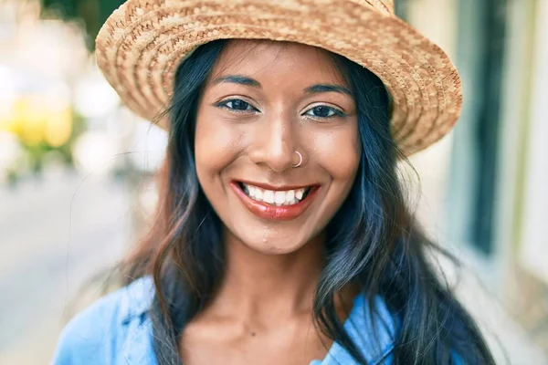 Young beautiful indian woman wearing summer hat smiling happy walking at the city.