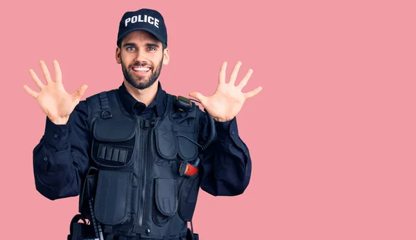 Young handsome man with beard wearing police uniform showing and pointing up with fingers number ten while smiling confident and happy.