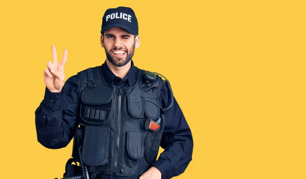 勝利サインをするカメラには幸せそうな顔をした笑顔で警官の制服を着た髭を生やした若いハンサムな男 — ストック写真