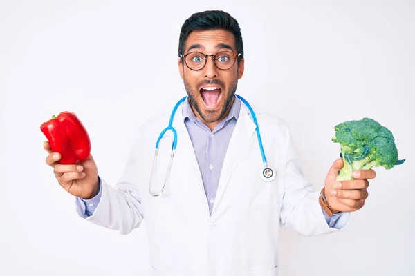 Jovem Hispânico Vestindo Estetoscópio Médico Segurando Pimenta Vermelha Brócolis Celebrando — Fotografia de Stock