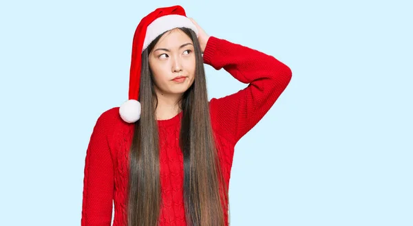 クリスマスの帽子を身に着けている若い中国の女性は混乱し 質問について疑問に思う 疑いもなく頭に手を置いて考える 包括的な概念は — ストック写真