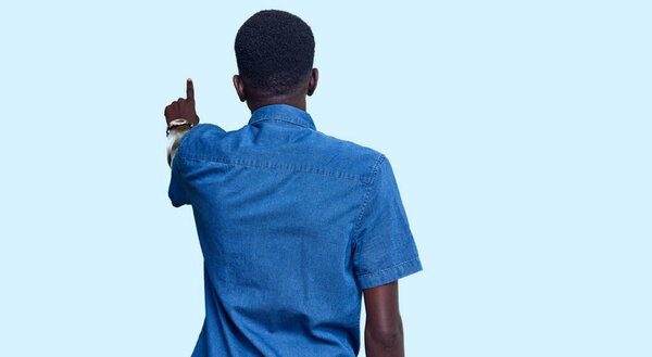 Young african american man wearing casual clothes posing backwards pointing ahead with finger hand