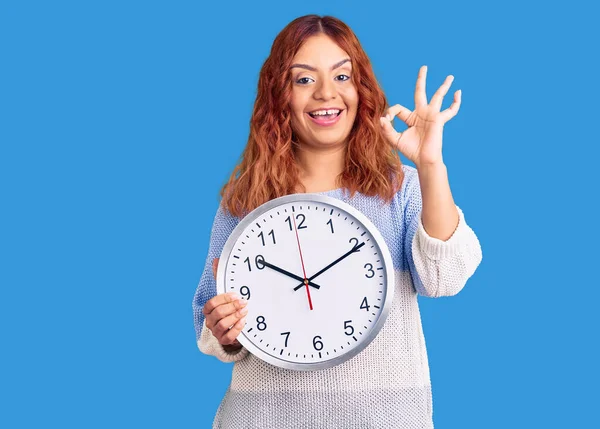 Young Latin Woman Holding Big Clock Doing Sign Fingers Smiling — Stock Photo, Image