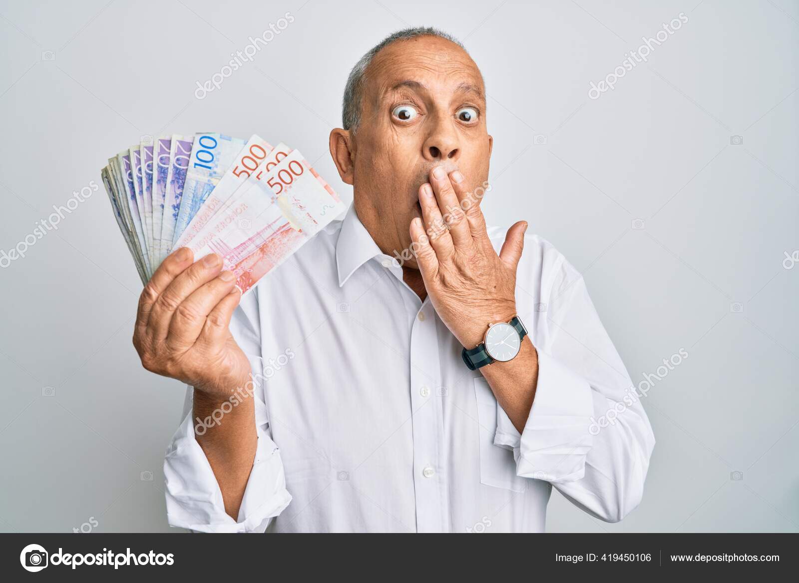 英俊的老人手里拿着瑞典克朗钞票捂着嘴惊恐万分生怕出错惊讶的表情——图库图片© Krakenimages.com #419450106