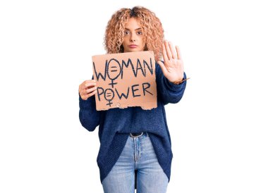 Sarışın, kıvırcık saçlı bir kadın. Değişiklik pankartı lazım. El açık, dur işareti yapıyor. 