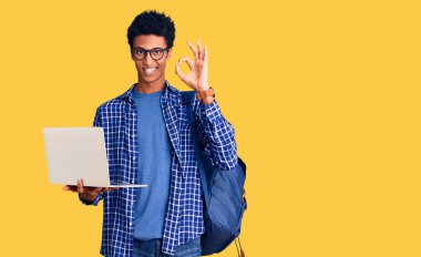 Genç Afro-Amerikalı bir adam sırt çantası tutuyor dizüstü bilgisayar kullanıyor. Parmaklarıyla imza atıyor, gülümsüyor. 