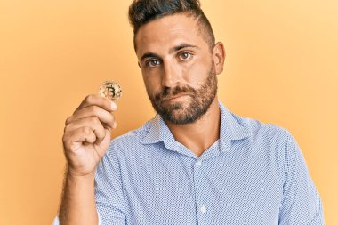 Sakallı yakışıklı bir adam sanal para birimini elinde tutuyor. Bitcoin düşünce tarzı ve kendine güveni olan ayık bir ifade. 