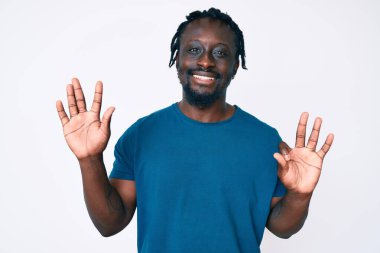 Saçları örgülü genç Afro-Amerikalı bir adam 8 numarayı gösterip gösterirken kendinden emin ve mutlu gülümsüyor.. 