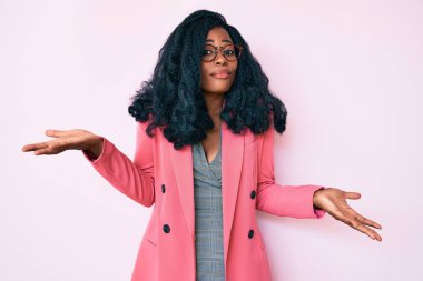 İş ceketi giyen, gözlüklü, kafası karışık kolları ve elleri havada güzel bir Afrikalı kadın. şüphe kavramı. 