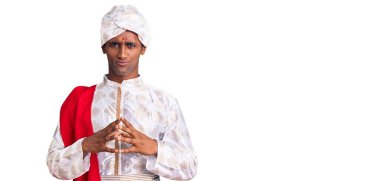 Geleneksel Sherwani sarisi giyen Afrikalı yakışıklı adam ellerini birleştiriyor ve gülümsüyor rahat ve neşeli. Başarı ve iyimserlik 