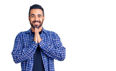 Gündelik kıyafetler giyen genç İspanyol adam elleriyle dua ediyor af diliyor kendinden emin bir şekilde gülümsüyor.. 