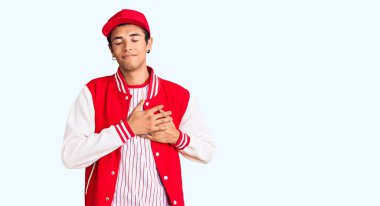 Beyzbol üniforması giyen, elleri göğsünde, gözleri kapalı gülümseyen ve yüzünde minnet ifadesi olan Afrikalı genç bir Amerikalı. sağlık kavramı. 