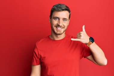 Yakışıklı, beyaz bir adam, günlük kırmızı tişört giyiyor, gülümsüyor, telefonla el ve parmak hareketleri yapıyor, telefonda konuşuyor gibi. iletişim kavramları. 