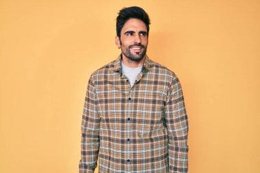 Yakışıklı, sakallı, sıradan kıyafetler giyen, yüzünde gülümseme ve doğal ifadeyle yan yana bakan İspanyol bir adam. Kendinden emin gülen. 