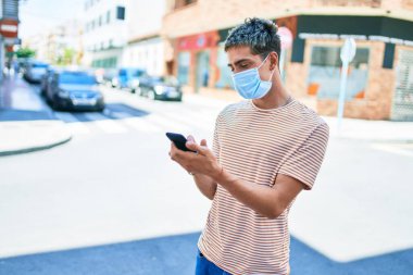 Coronavirus protencion tıbbi maske takan yakışıklı beyaz adam şehirde akıllı telefon kullanarak yürüyor..