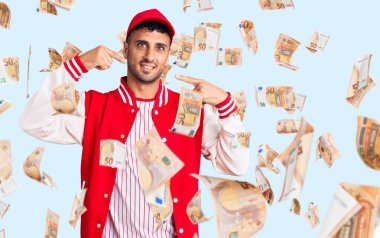 Beyzbol forması giyen, neşeli gülümseyen, parmaklarını ve ağzını gösteren genç bir İspanyol. diş sağlığı kavramı.