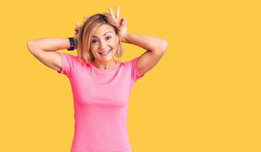 Spor giyinen genç sarışın kadın komik ve çılgın pozlar veriyor parmakları tavşan kulağı gibi, neşeli bir şekilde gülümsüyor. 