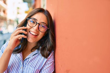 Genç İspanyol iş kadını gülümsüyor. Şehirdeki akıllı telefondan mutlu bir şekilde konuşuyor..