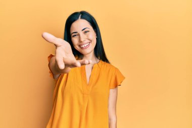 Güzel, genç bir bayan günlük giysiler içinde gülümseyerek selamlama ve hoş geldin demek için el sıkışmayı teklif ediyor. başarılı iş. 