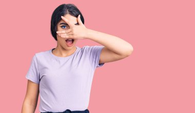 Esmer, sıradan kıyafetler giyen genç kız şok içinde yüzünü ve gözlerini kapayarak utangaç ifadesiyle parmaklarının arasından bakıyor.. 