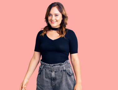 Genç, güzel, beyaz bir kadın günlük kıyafetler giyiyor. Pozitif ve mutlu görünüyor. Kendine güvenen bir gülümsemeyle dişlerini gösteriyor. 