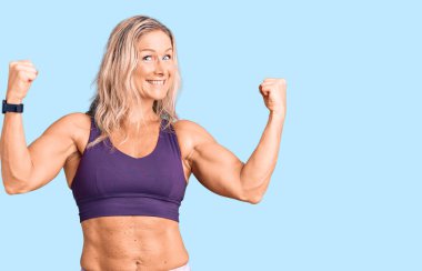 Orta yaşlı sarışın kadın spor kıyafetleri giyiyor gururla bağırıyor zaferi ve başarıyı kutluyor kollarını kaldırarak heyecanlanıyor. 