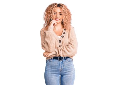 Kış kazağı giyen kıvırcık saçlı genç sarışın kadın kameraya kendinden emin bakıyor kolları çapraz ve çenesi açık gülümsüyor. Olumlu düşünmek. 