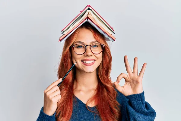 Молодая Рыжая Женщина Держит Книги Над Головой Делает Хорошо Знак — стоковое фото