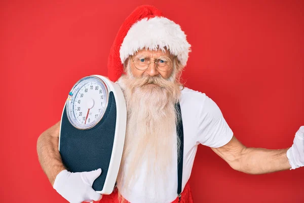Old senior man on diet wearing traditional santa claus costume annoyed and frustrated shouting with anger, yelling crazy with anger and hand raised